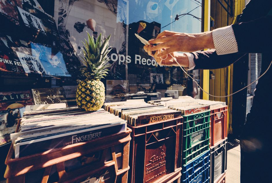 Man using a smartphone outside a record shop with vinyl crates and a pineapple. Urban lifestyle captured.