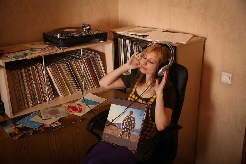Woman sitting with headphones, surrounded by vinyl records, enjoying music in a vintage setting.